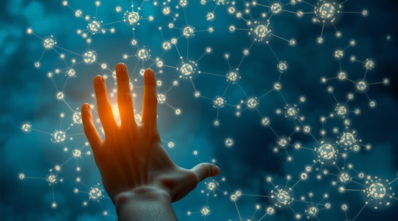 Rozświetlona dłoń sięga w kierunku skomplikowanej, półprzezroczystej sieci neuronowej spowitej mgłą na tle głębokiego błękitu.